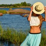 Woman enjoys a summer day by the rocky beach in Helsinki, hiding face with a straw hat